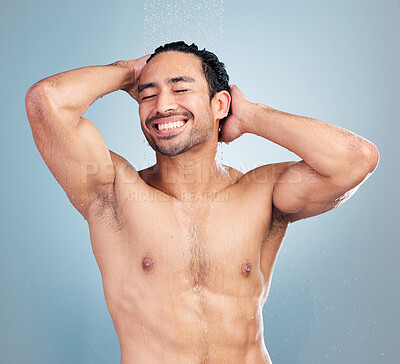 Buy stock photo Smiling muscular asian man showering alone in a studio and washing his hair against a blue background. Fit and strong mixed race man standing under pouring water. Hispanic athlete enjoying hot shower