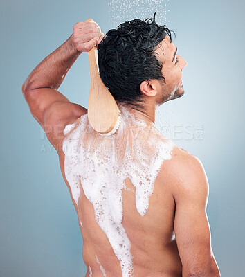 Buy stock photo Young mixed race man taking a warm shower washing his back with a shower brush against a blue studio background. Happy hispanic guy washing his body with soap and doing his morning grooming routine