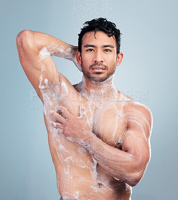 Buy stock photo Portrait of a muscular young mixed race man taking a warm shower against a blue studio background. Serious hispanic guy washing hair and body with soap under clean running water for good hygiene