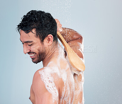 Buy stock photo Closeup of a smiling man taking a warm shower washing his back with a shower brush against a blue studio background. Mixed race male washing his body with soap scrubbing his back doing morning grooming routine