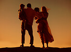 Caucasian family watching the sunset standing on a rock together on the beach from behind. Parents spending time with their son and daughter on holiday. Siblings bonding with mom and dad on vacation


