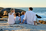Carefree caucasian family watching the sunset sitting on a rock together on the beach. Parents spending time with their son and daughter on holiday. Siblings bonding with mom and dad on vacation