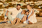 Portrait of happy caucasian family watching the sunset sitting on a rock together with cityscape view in background. Cheerful parents spending time with their son and daughter on holiday