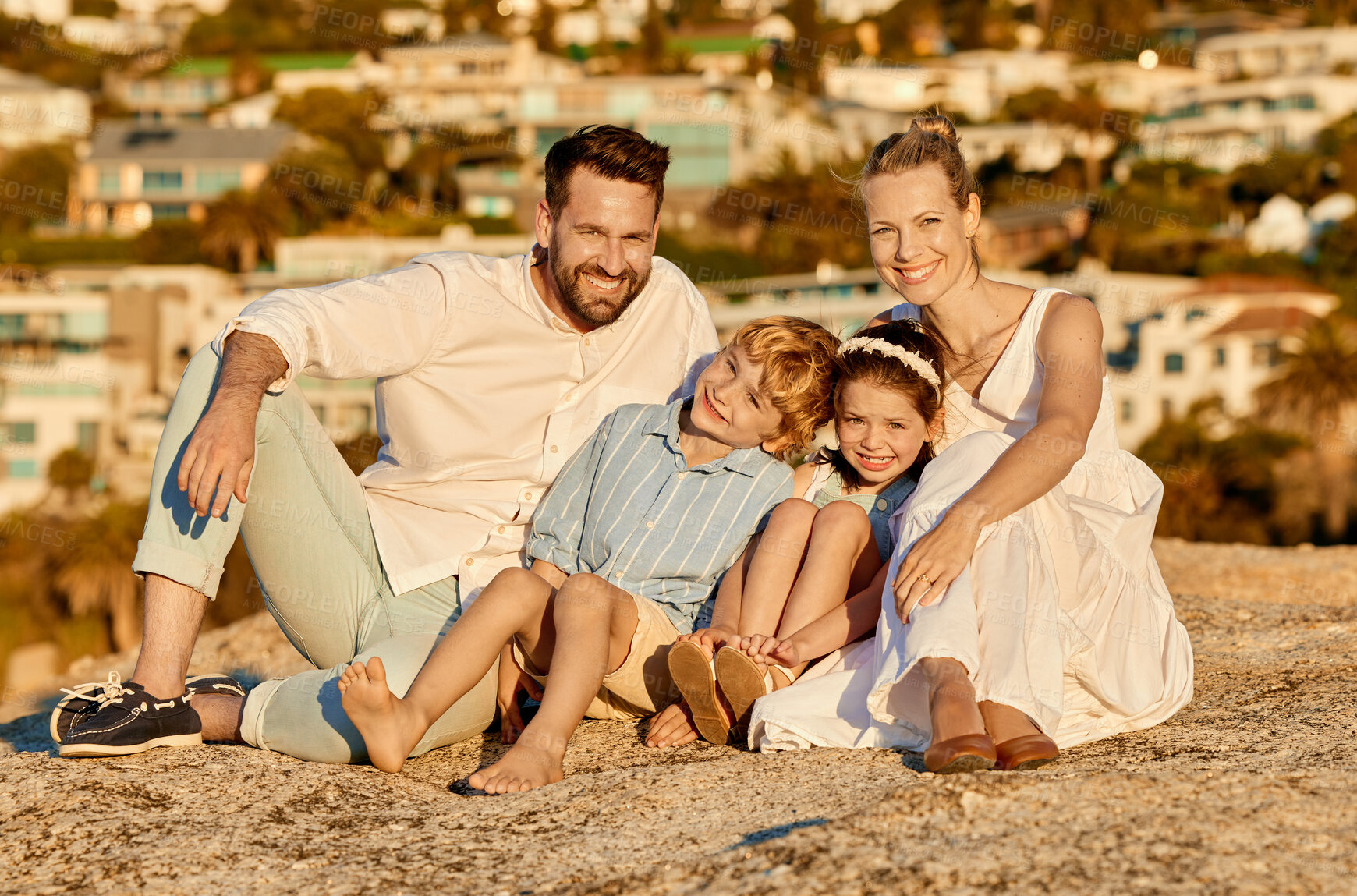 Buy stock photo Portrait of happy caucasian family watching the sunset sitting on a rock together with cityscape view in background. Cheerful parents spending time with their son and daughter on holiday