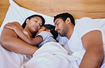 Mixed race family of three asleep in bed. Above mother, father and daughter resting on a white bed in the bedroom at home. Tired parents lying in bed sleeping with their daughter in the middle 