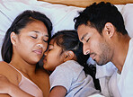 Mixed race family, mother, father and daughter resting on the white bed in the bedroom at home. Tired parents lying in bed sleeping with their daughter in the middle
