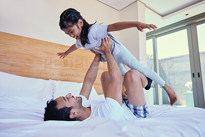 Buy stock photo Young dad lifting his daughter in the air while lying on bed. Cheerful father playing with adorable little daughter and enjoying a family weekend together. Loving and caring dad practising acroyoga with child 