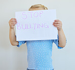 Little girl holding a paper with message that bullying at school must be stopped. Blonde child actively protest against bullying, kid starting an anti bully campaign against white copyspace background