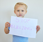 Little girl protesting against bullying with a sign. Adorable caucasian child standing alone and holding a protest poster against white background. Kid campaigning against bullying
