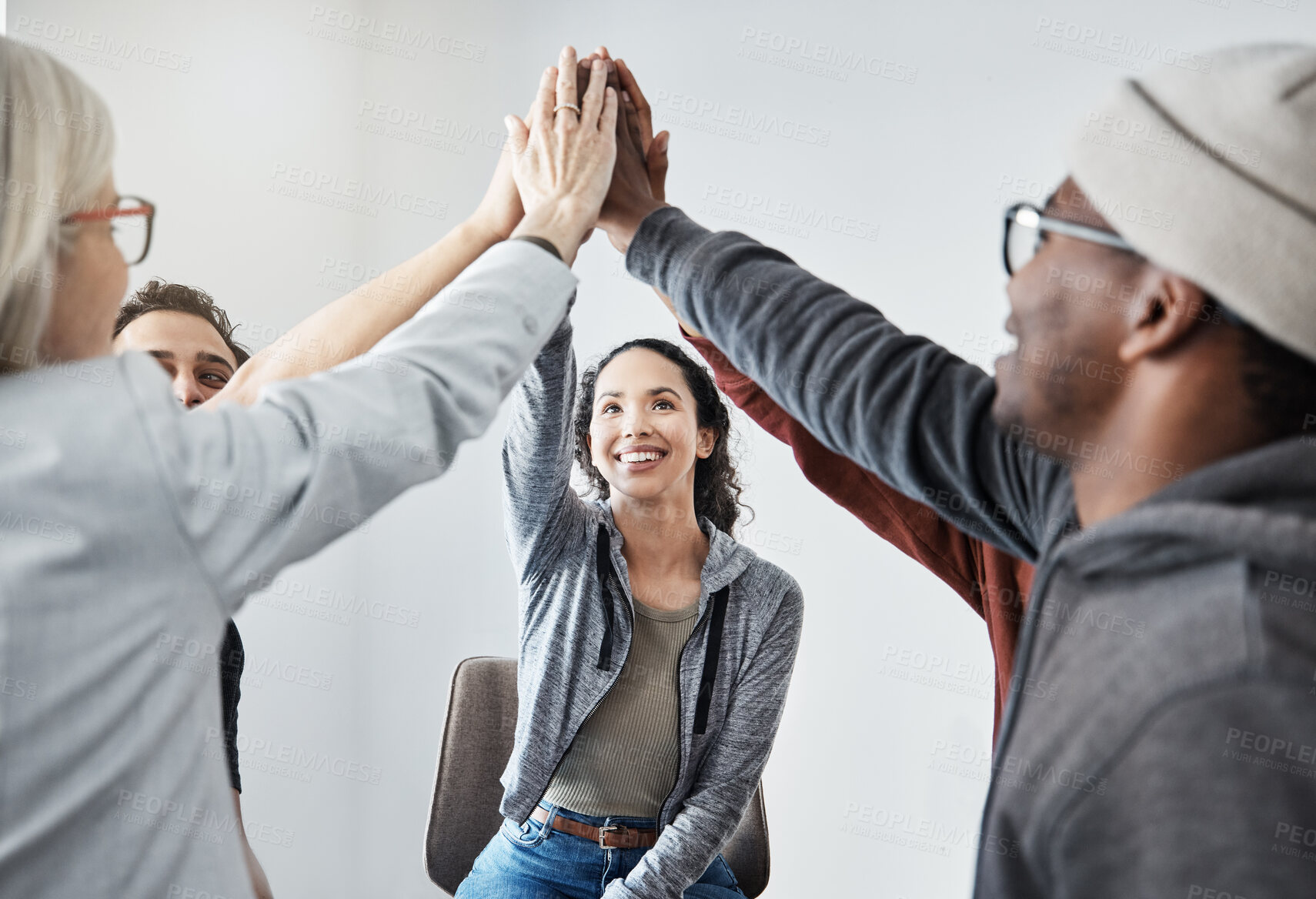 Buy stock photo Happy diverse group of businesspeople smiling giving each other a high five sitting in a meeting in an office at work. Happy women and men joining their hands for motivation while working together

