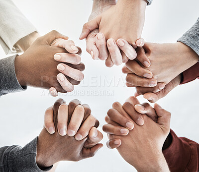 Buy stock photo Below close up  view of people holding hands in circle shape. A group of people putting their hands together while standing in a huddle inside against a clear grey background. Anything is possible with teamwork