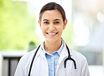 Confident young mixed race female doctor standing and smiling inside a medical office. One hispanic woman in a white coat with stethoscope. Trusted practitioner caring for the health of patients