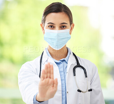 Portrait of a hispanic female doctor wearing a mask and showing a stop gesture with her hand while wearing a stethoscope in a hospital office.