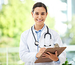 Confident young mixed race female doctor standing with clipboard a medical office. One hispanic woman in a white coat with stethoscope. Trusted practitioner caring for the health of patients