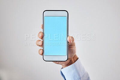 Buy stock photo Closeup of man holding mobile phone with blue blank screen in hand against grey studio background. Space for website or mobile app design. Cellphone smartphone display mockup
