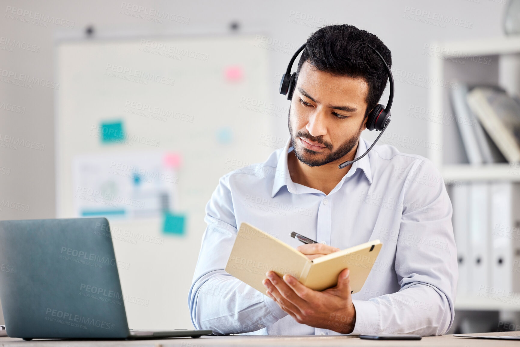 Buy stock photo Asian call center agent writing notes while using a laptop in an office. Mixed race customer service representative wearing a headset and listening to customer. Intern businessman on a conference call