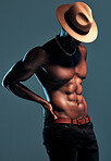 Fashionable african American model posing shirtless against blue studio background with copyspace. Sexy, unknown black man with attitude showing bare six pack while wearing hat. Masculine and muscle