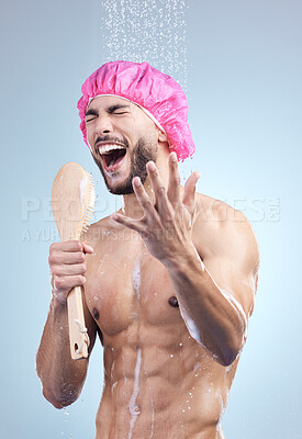 Handsome young man wearing a pink bonnet singing in the shower. Happy mixed race male holding shower brush while rinsing soap off his body under clean running water. Handsome hunk doing his morning self-hygiene and body care routine