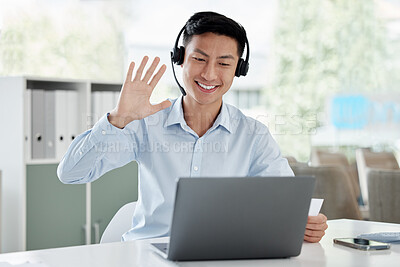 Happy asian business man in headset waving at webcam during video conference on laptop. Positive young guy in headset learning foreign language and greeting during video call in his office