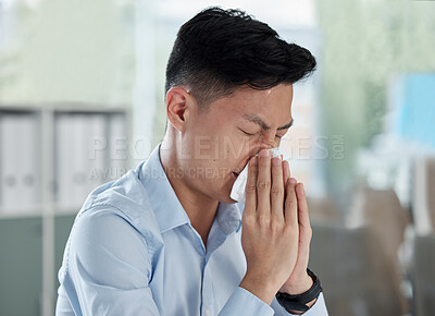 One sick asian businessman blowing runny nose with tissue while working in an office. Guy feeling unwell with flu, cold and covid symptoms. Suffering with congestion, sinus and seasonal spring allergy