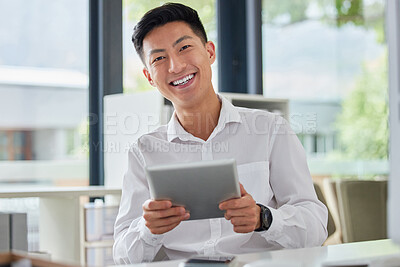 Young happy asian businessman using social media on a digital tablet sitting in an office at work. One chinese man smiling checking an email on a digital tablet. Man sending a message on a tablet