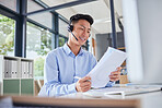 Asian translator or business man with headset smiling while sitting in office. Accountant checking documents, preparing financial report. Friendly call centre agent sitting at his desk 