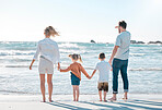 Carefree caucasian family walking and holding hands together on the beach. Parents spending time with their son and daughter on holiday. Little siblings holding hands with their parents on vacation