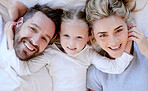 Portrait of happy carefree caucasian family in pyjamas from above lying cosy together in bed at home. Loving parents with little daughter. Cute young girl touching and hugging her mom and dad's face