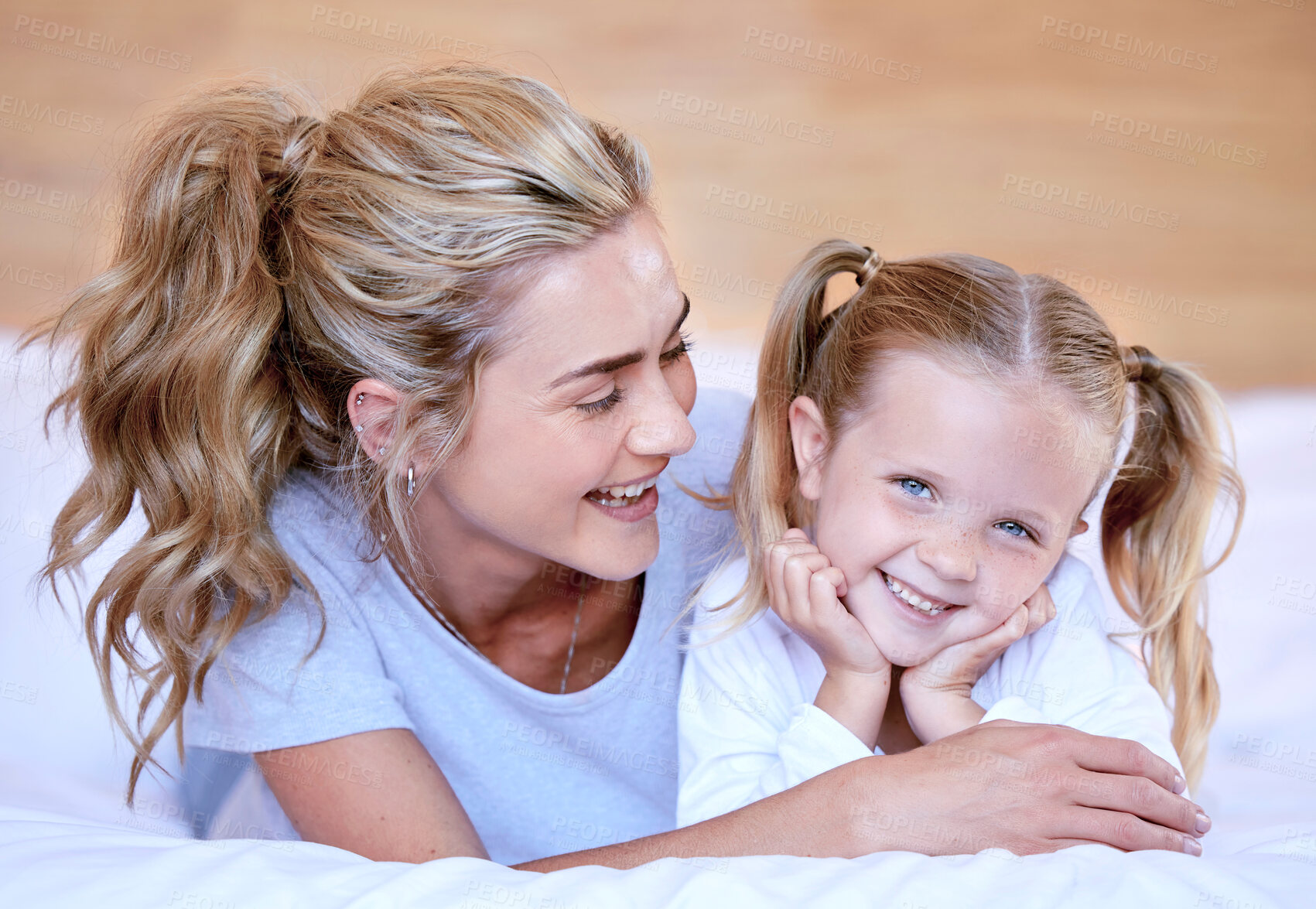 Buy stock photo Happy caucasian mother and daughter lying on a bed at home. Cheerful woman with cute little girl enjoying a cosy and lazy relaxing day together. Loving parent bonding and sharing quality time with kid