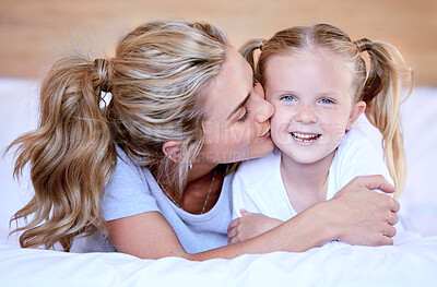 Two blonde caucasian females only looking relaxed and positive while lying in bed together. Young single mother kissing her adorable little daughter on an comfortable bed in a bright bedroom