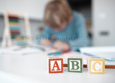 Buy stock photo Closeup of wooden toy blocks on a table at home. A little boy blurred in the background, playing, doing his homework and getting an education through distance learning