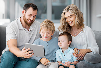 Happy relaxed family of four using a digital tablet device while bonding on the sofa together at home. Young couple checking social media and watching a movie with their two cute caucasian sons
