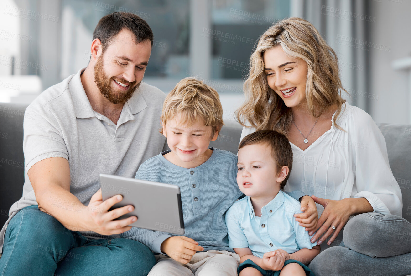 Buy stock photo Happy relaxed family of four using a digital tablet device while bonding on the sofa together at home. Young couple checking social media and watching a movie with their two cute caucasian sons 
