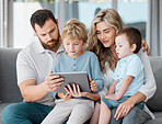 Loving family with two kids sitting at home with device. Caucasian parents and little children using digital tablet looking at screen sitting on sofa together. Family watching cartoon movie online