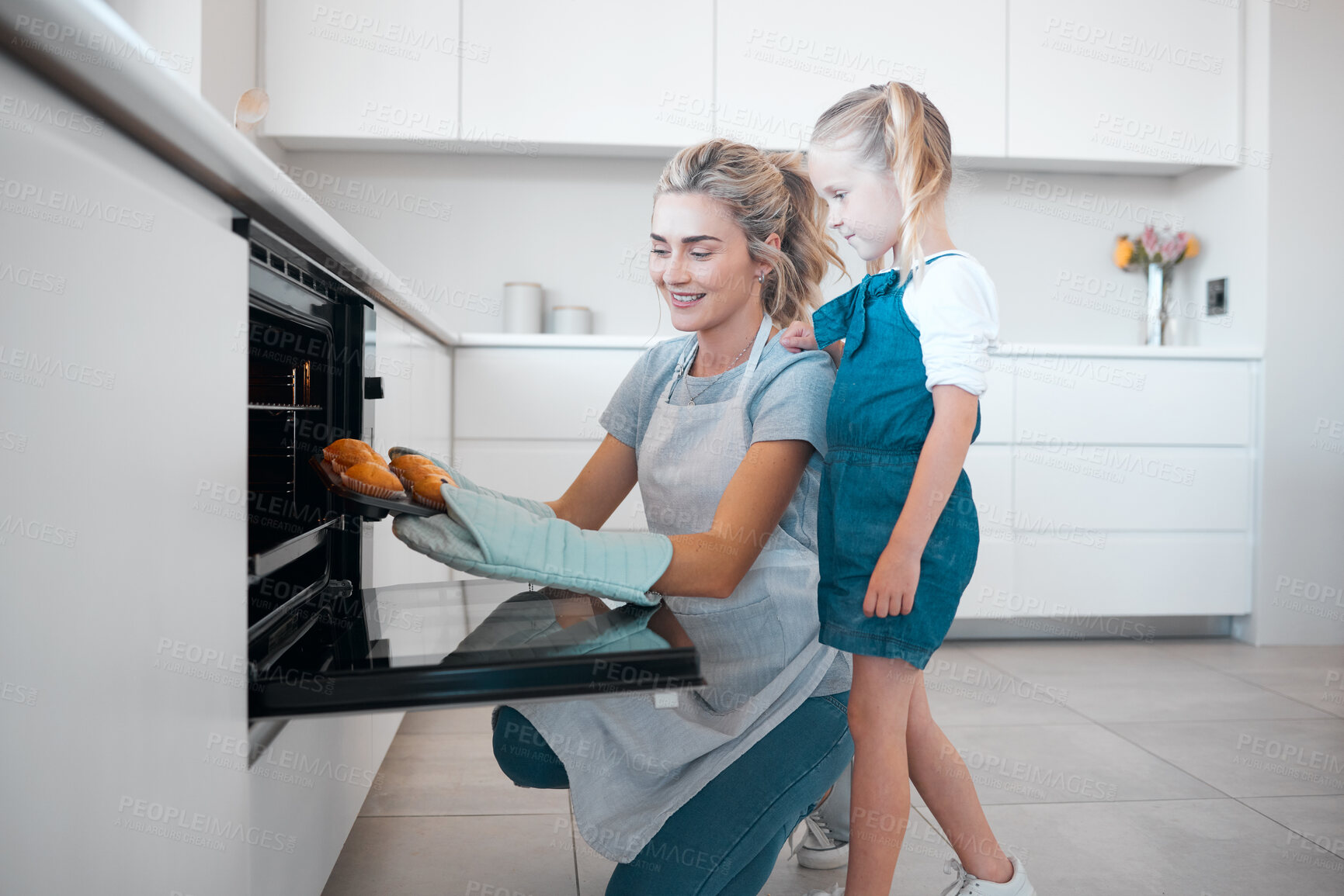Buy stock photo mother and daughter removing a tray of fresh baked muffins from the oven.Little girl and her mother baking together. Happy mother and daughter removing baked dessert muffins from the oven