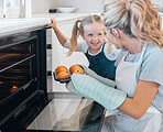 Happy mother and daughter removing muffins from the oven. Little girl looking at her parent holding a tray of muffins.Smiling caucasian girl making dessert muffins with her mother.