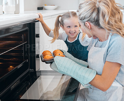 Buy stock photo Happy mother and daughter removing muffins from the oven. Little girl looking at her parent holding a tray of muffins.Smiling caucasian girl making dessert muffins with her mother.