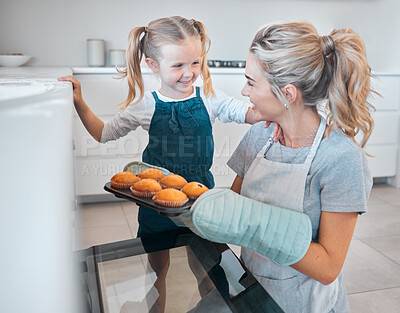 Mother and daughter removing tray of muffins from the oven. Happy woman baking muffins with her daughter. Little girl bonding with her mother and baking. Parent taking muffins from the oven
