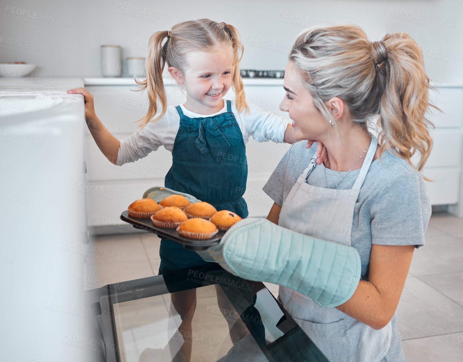 Buy stock photo Mother and daughter removing tray of muffins from the oven. Happy woman baking muffins with her daughter. Little girl bonding with her mother and baking. Parent taking muffins from the oven
