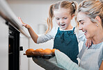 Happy mother and daughter looking at muffins. Young woman removing a tray of fresh, baked muffins from the oven. Smiling woman holding a tray of muffins. Mother and daughter bonding in the kitchen