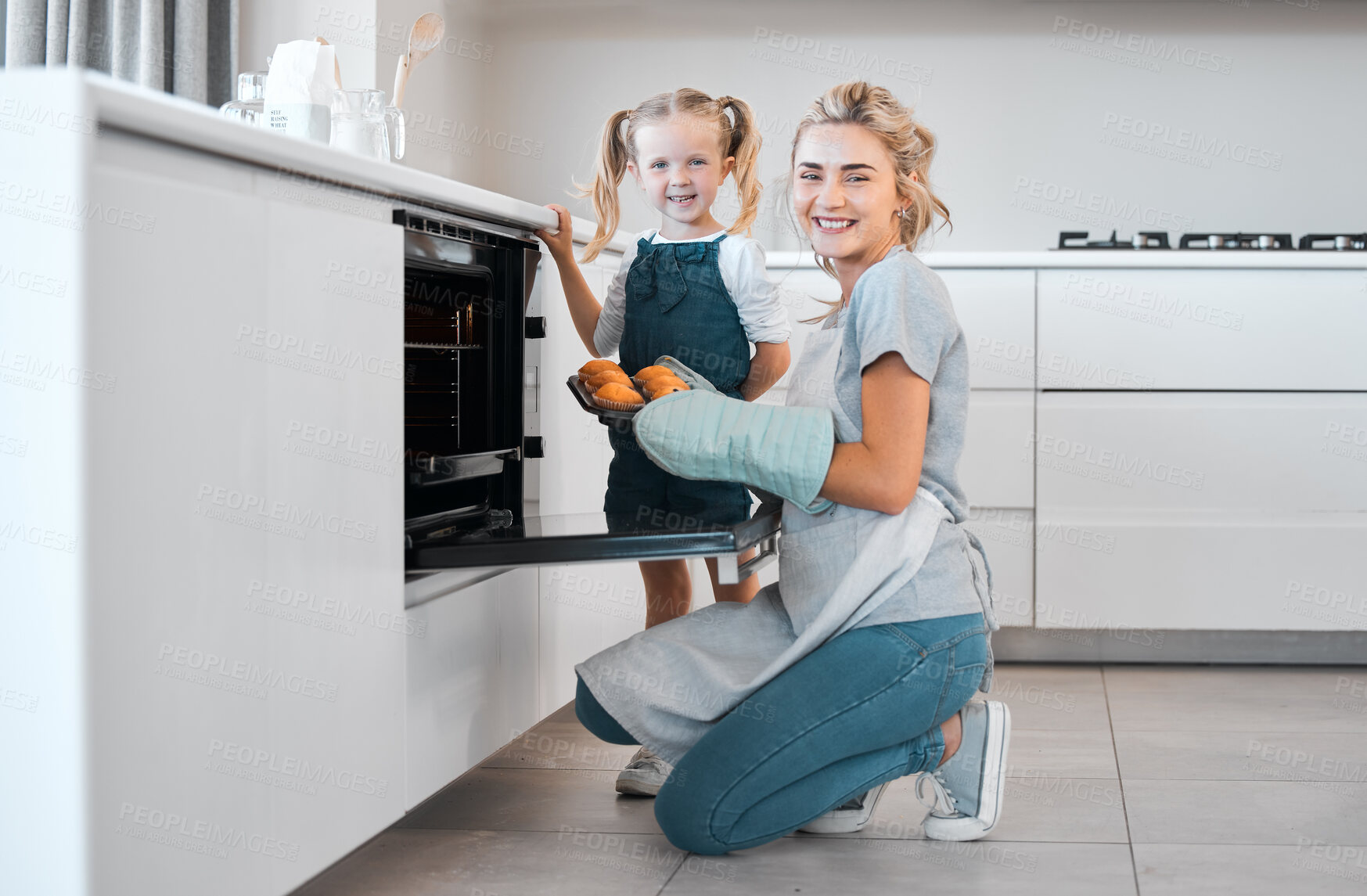 Buy stock photo Smiling mother and daughter baking together. Happy parent and child holding tray of baked muffins.Caucasian woman taking fresh, baked muffins out of the oven. Portrait of a mother and daughter baking