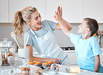 Cheerful mother giving her son a high five. Happy mother and son baking together. Caucasian mother motivating her son while they bake together. Mother celebrating and baking with her son