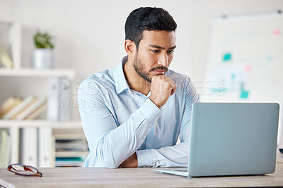 Buy stock photo Young serious mixed race businessman sitting at a table working on a laptop alone in an office at work. One hispanic male boss reading and sending emails on a laptop