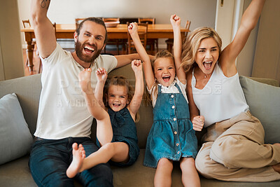 Young happy caucasian family cheering in support sitting together on the couch at home. Joyful little sisters celebrating with their mother and father. Excited parents cheering with joy with their daughters