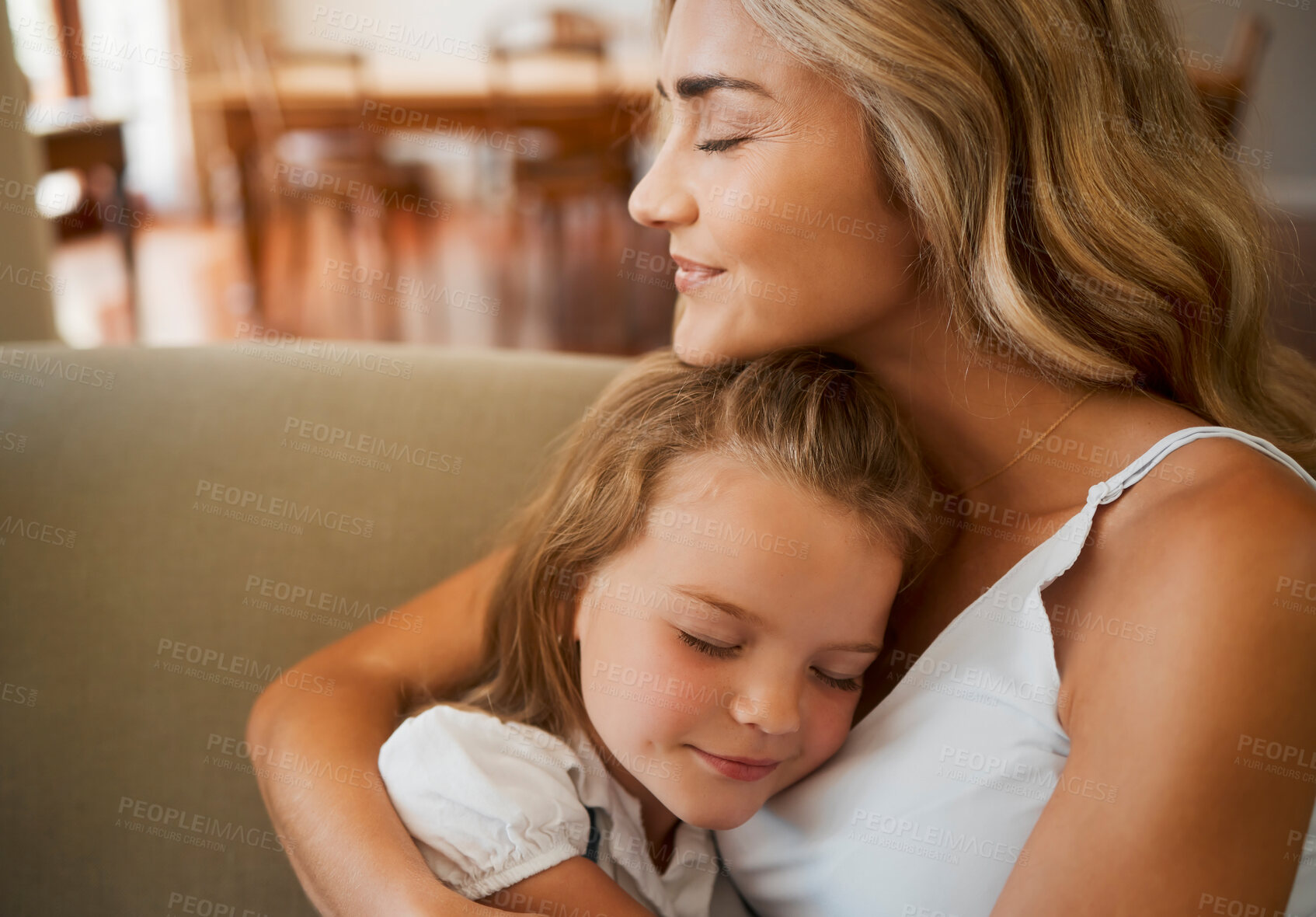 Buy stock photo Young loving caucasian mother hugging her little daughter relaxing and sitting on the couch together at home. Innocent carefree girl embracing her mom resting on the couch