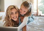Happy young caucasian mother and daughter using a digital tablet together relaxing on a bed at home. Cute little girl taking a selfie with a digital tablet with her mom
