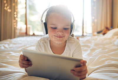 Little girl with digital tablet and headphones on the bed at home. Cute child looking happy while watching cartoons with music on device or doing a video call
