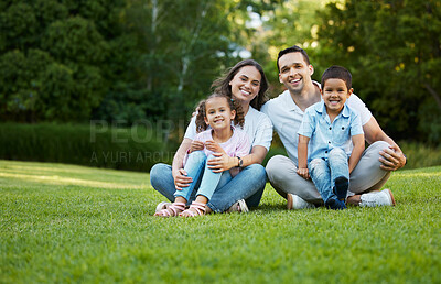 Buy stock photo Portrait of carefree mixed race family spending time together at park. Happy parents with son and daughter bonding and having fun outdoors. Young couple sitting with two children sitting on grass