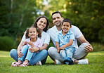 Young happy mixed race family relaxing and sitting on grass in a park together. Loving parents spending time with their little children in a garden. Carefree siblings bonding with their mom and dad