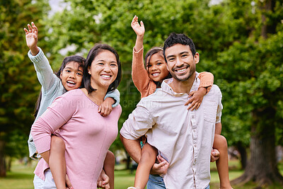 Mixed race family in the park. Happy young mother and father piggybacking their son and daughter outside. Couple carrying their kids while walking on grass during. Two sisters on parents\' backs